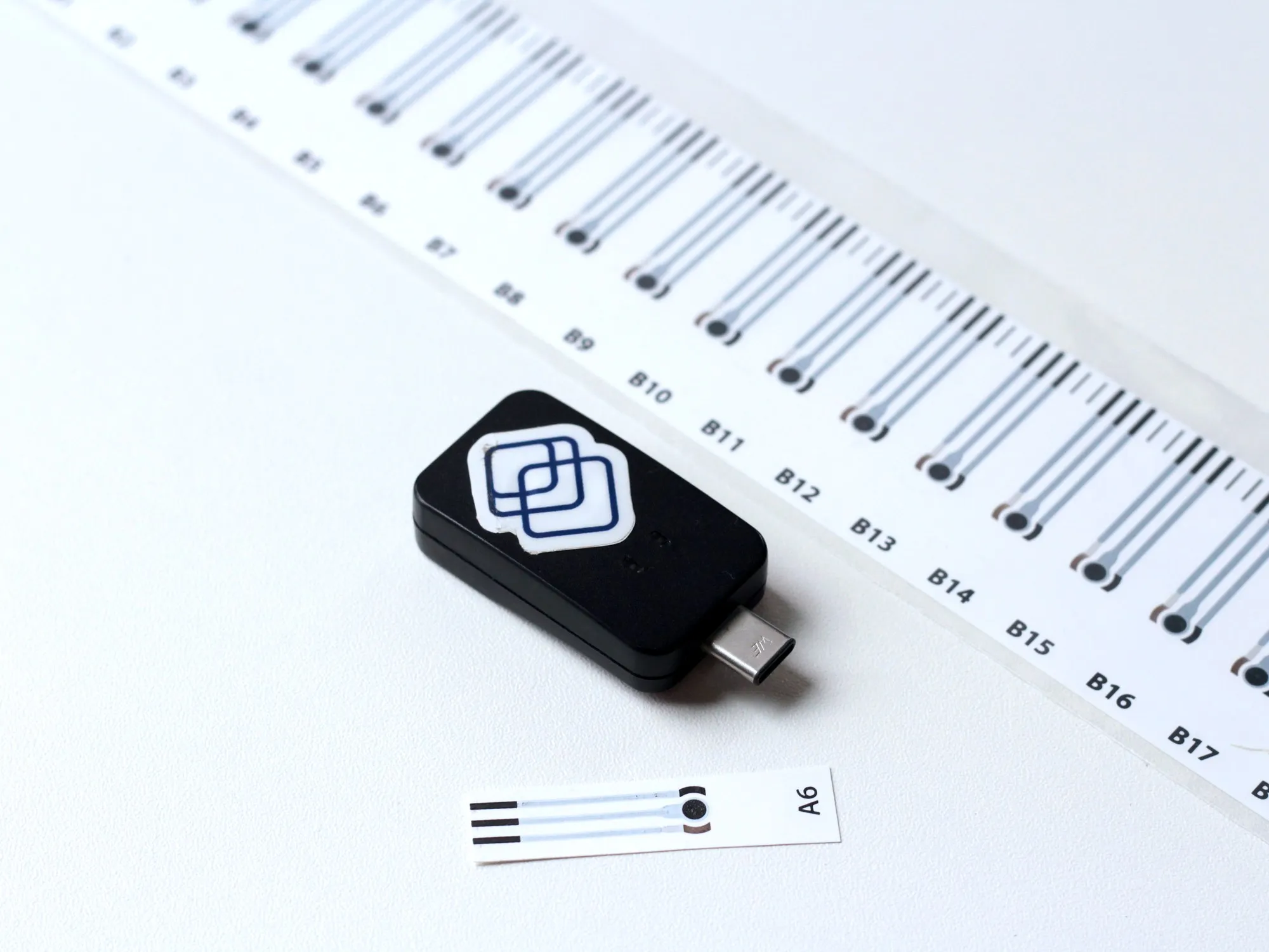 Segura reader alongside a single sensor strip and a full roll of barcoded strips
